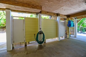 A covered outdoor area with a concrete floor, a yellow door, and a green hose coiled on the floor. - AMAZING HOME in Four Seasons in Duck! Private Pool! 10% OFF available summer weeks! (Duck)