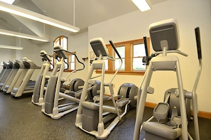 A row of treadmills in a gym with a window and a ceiling light fixture. - AMAZING HOME in Four Seasons in Duck! Private Pool! 10% OFF available summer weeks! (Duck)