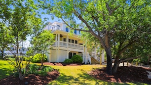 A two-story house with a balcony, surrounded by trees and a well-maintained lawn. - AMAZING HOME in Four Seasons in Duck! Private Pool! 10% OFF available summer weeks! (Duck)