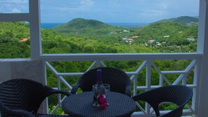 Un balcon agrémenté de fauteuils et d’une table en osier, offrant une vue imprenable sur un paysage verdoyant et la mer.