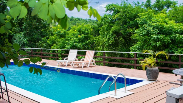 Une terrasse en bois avec une piscine, entourée d’une végétation luxuriante et d’une clôture en bois.