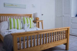 A wooden bed with green and white striped pillows, a bedside table with a lamp, and a white wardrobe with louvered doors.