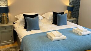 Ein ordentlich bezogenes Bett mit weißer und blauer Bettwäsche, zwei Nachttische mit Lampen, ein flauschiger Teppich und eine Holzbank.