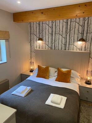 Een slaapkamer met een groot bed, twee nachtkastjes, een hoofdbord met behang van bomen en twee wandlampen.