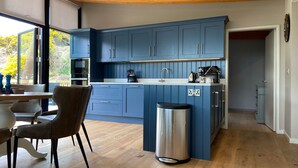 Eine moderne Küche mit blauen Schränken, einem Mülleimer aus Edelstahl und einem Essbereich mit einem Holztisch und Stühlen.