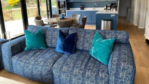 Ein modernes Wohnzimmer mit einem blauen, gemusterten Sofa, türkisfarbenen Kissen und einem Essbereich mit rundem Tisch und Stühlen.