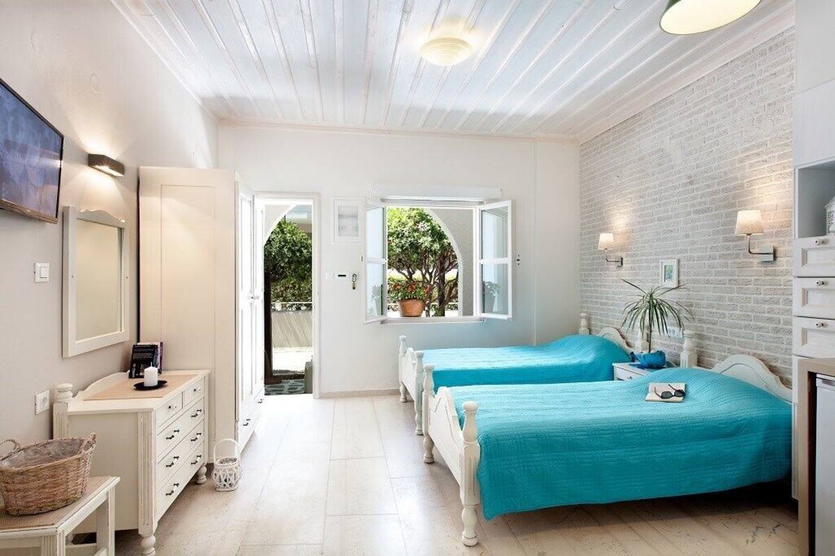 A bedroom with two beds, a white dresser, a mirror, and a brick wall.