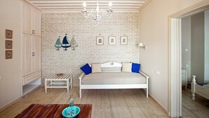 A room with a white bed, a small table, a bench, and a chandelier. - Alkionides Seaside Apartments (Platanias)
