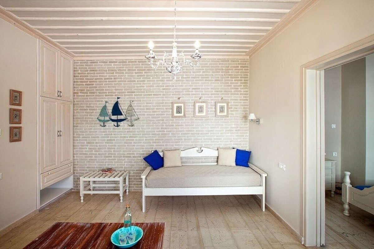 A room with a white bed, a small table, a bench, and a chandelier.