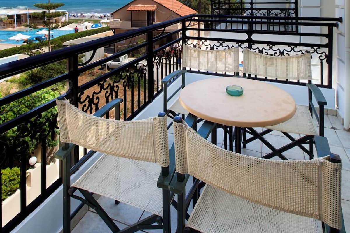 A balcony with a view of the sea, a table, and two wicker chairs.