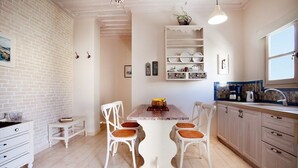 A kitchen with white cabinetry, a wooden dining table with four chairs, and a hanging light fixture. - Alkionides Seaside Apartments (Platanias)