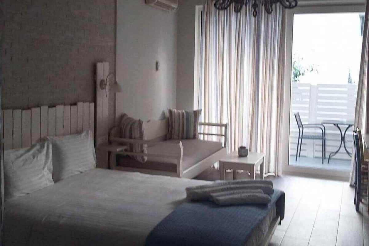 A bedroom with a large bed, a sofa, a small table, and a balcony with chairs.