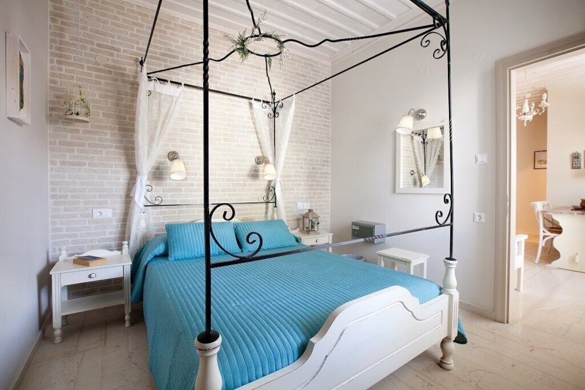 A bedroom with a four-poster bed, white walls, a brick accent wall, and a white ceiling.