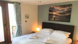 A neatly made bed with towels, a painting of a sunset, and a nightstand with a lamp. - Stables 3 -  a llyn peninsula that sleeps 2 guests  in 1 bedroom (Pwllheli)
