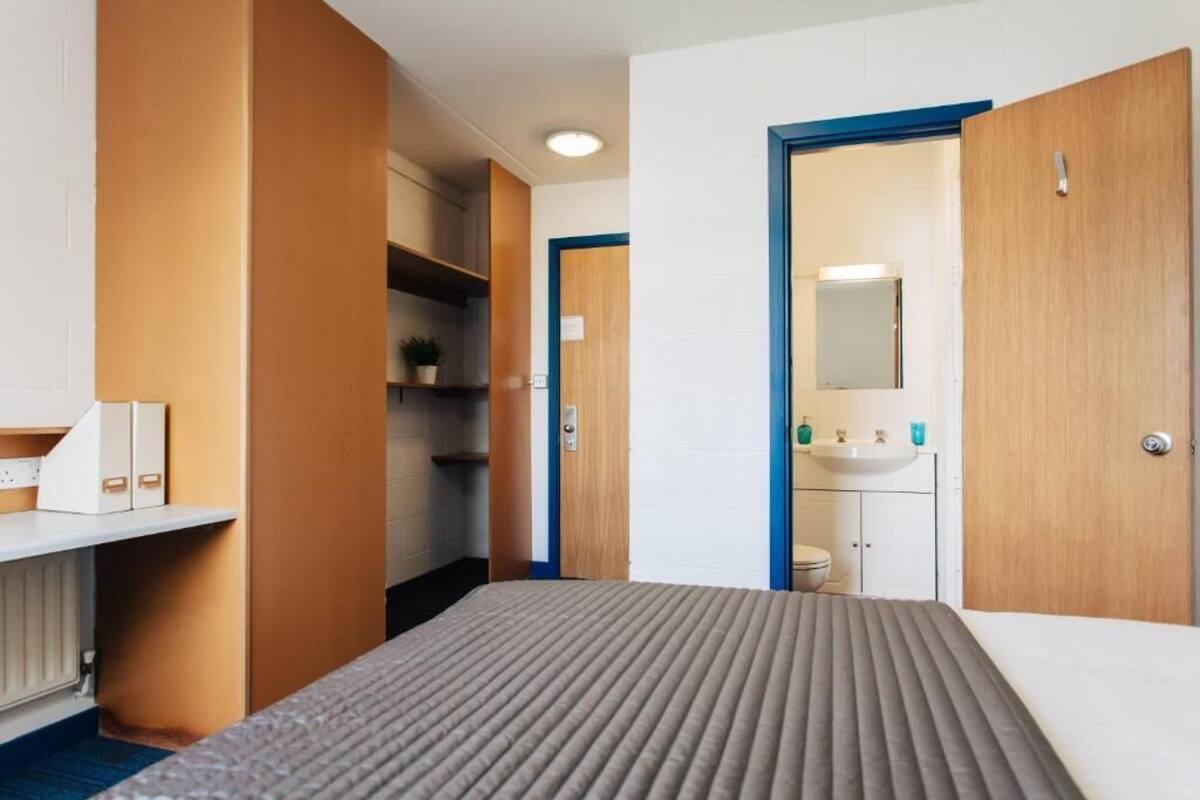 Una habitación de hotel con cama, mesita de noche, armario y baño con lavabo y espejo.