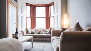 A cozy living room with a beige sofa, a coffee table, and a large window with wooden shutters.