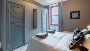 A hotel room with a bed, a window with curtains, a door, and a wall-mounted mirror.