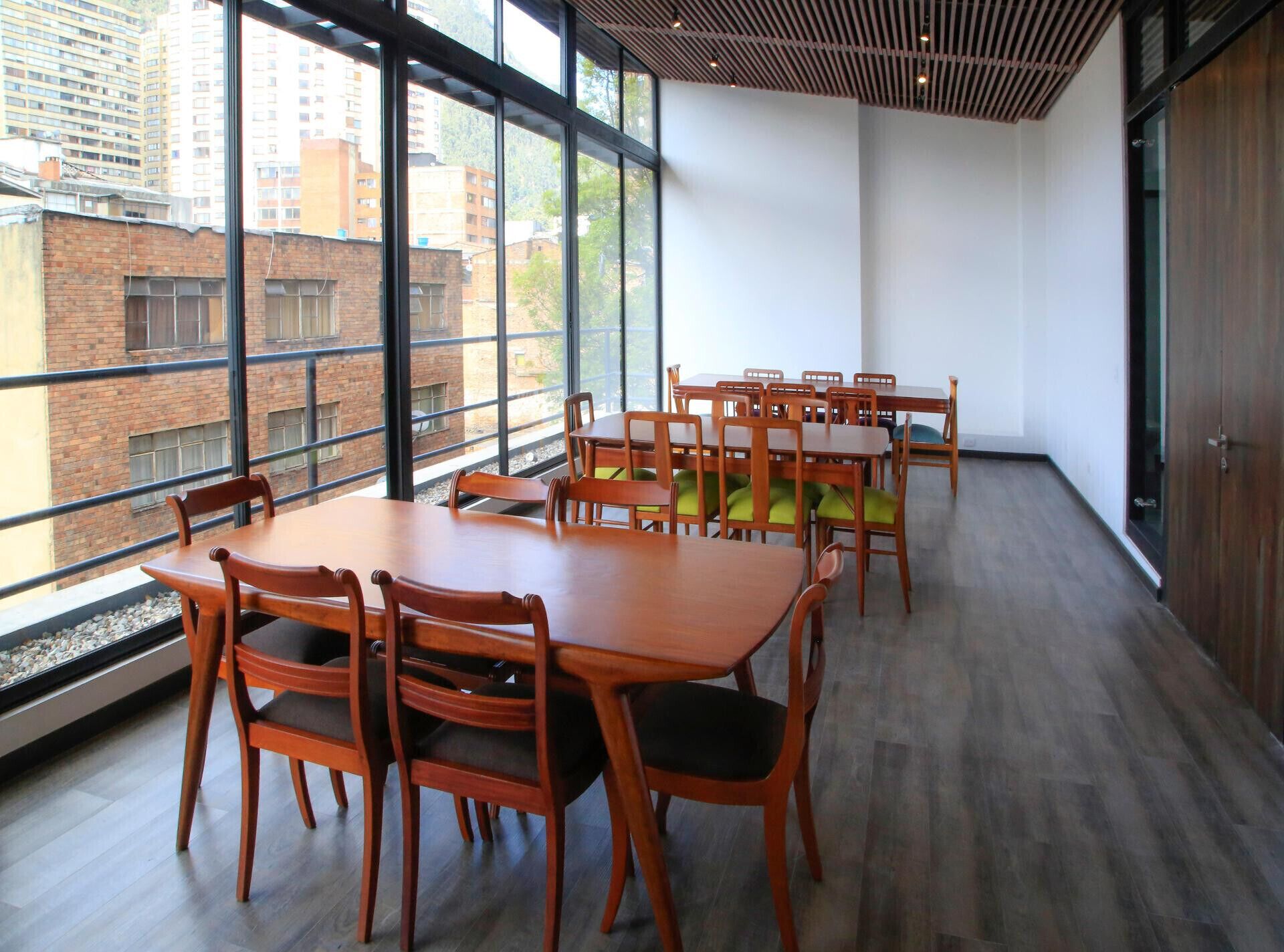 Una sala de conferencias con una gran mesa y sillas, ventanas amplias con vista a edificios, y techo de madera.
