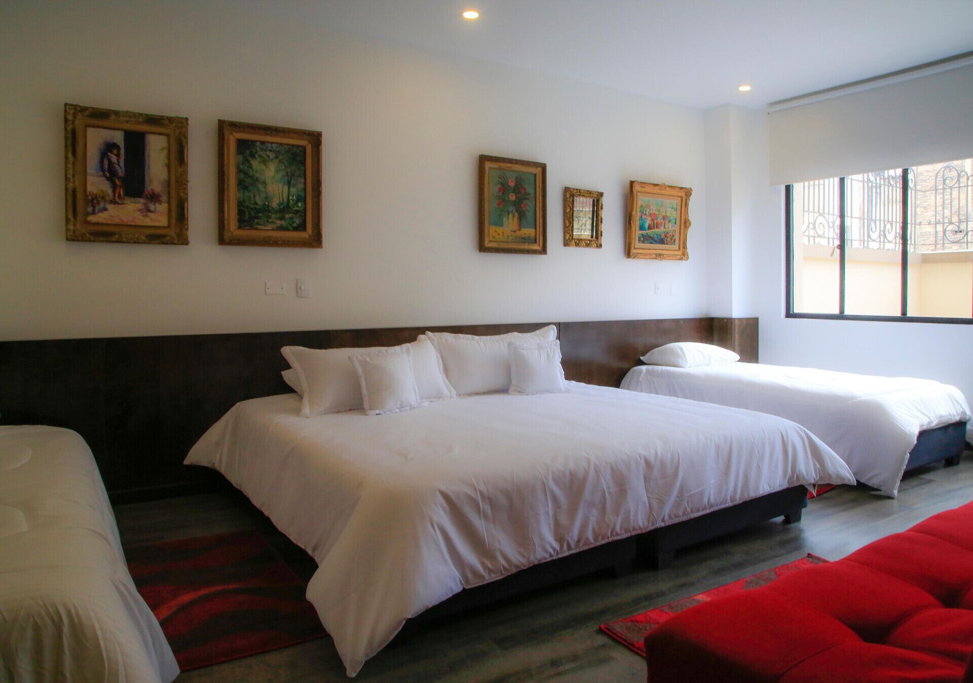 A hotel room with a large bed, two smaller beds, and a red accent rug.