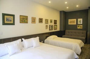A hotel room with two beds, a gray sofa, and a wall adorned with framed pictures.