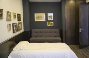 Una habitación con cama, sofá y una puerta. Hay cuadros enmarcados en la pared.