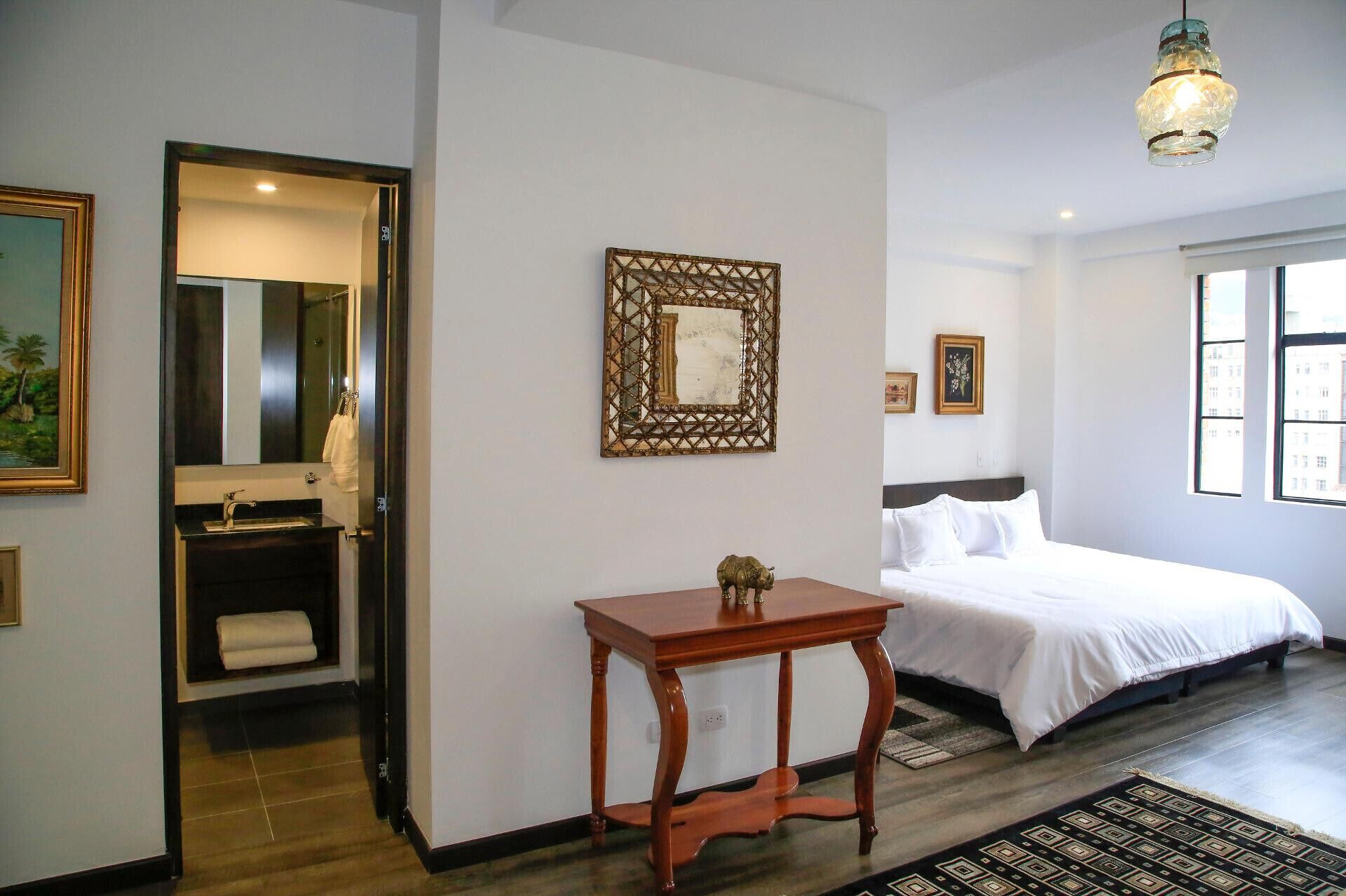 A hotel room with a bed, a bedside table, a mirror, and a window.