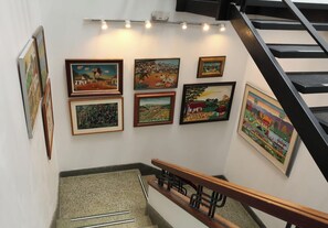 A staircase with a handrail and a wall displaying various framed artworks. - Hotel Museo San Moritz (Bogotá)