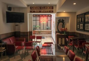 A hotel lobby with a red sofa, multiple red chairs, a glass coffee table, and a TV mounted on the wall.