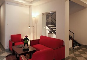 A modern living room with a red sofa, a small table, and a floor lamp. - Hotel Museo San Moritz (Bogotá)