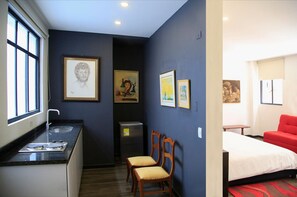 A hotel room with a bed, a desk with a sink, two chairs, and artwork on the walls.