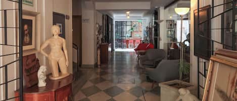 A hallway with a checkered floor, a statue on a cabinet, and a red chair in the distance.