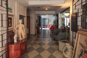 A hallway with a checkered floor, a statue on a cabinet, and a red chair in the distance. - Hotel Museo San Moritz (Bogotá)