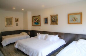 A hotel room with two single beds and a larger bed, all with white linens. There are four framed floral paintings on the wall. - Hotel Museo San Moritz (Bogotá)