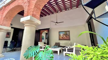 Un espacio de estar al aire libre cubierto, con arcos de ladrillo, muebles blancos y plantas verdes.