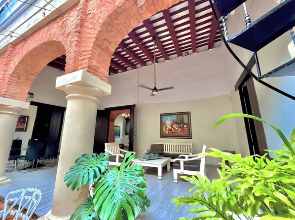 A covered outdoor seating area with brick arches, white furniture, and green plants.