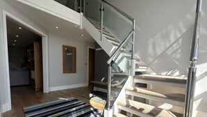Una escalera moderna con barandillas de vidrio y un tapete a rayas que lleva a un dormitorio.