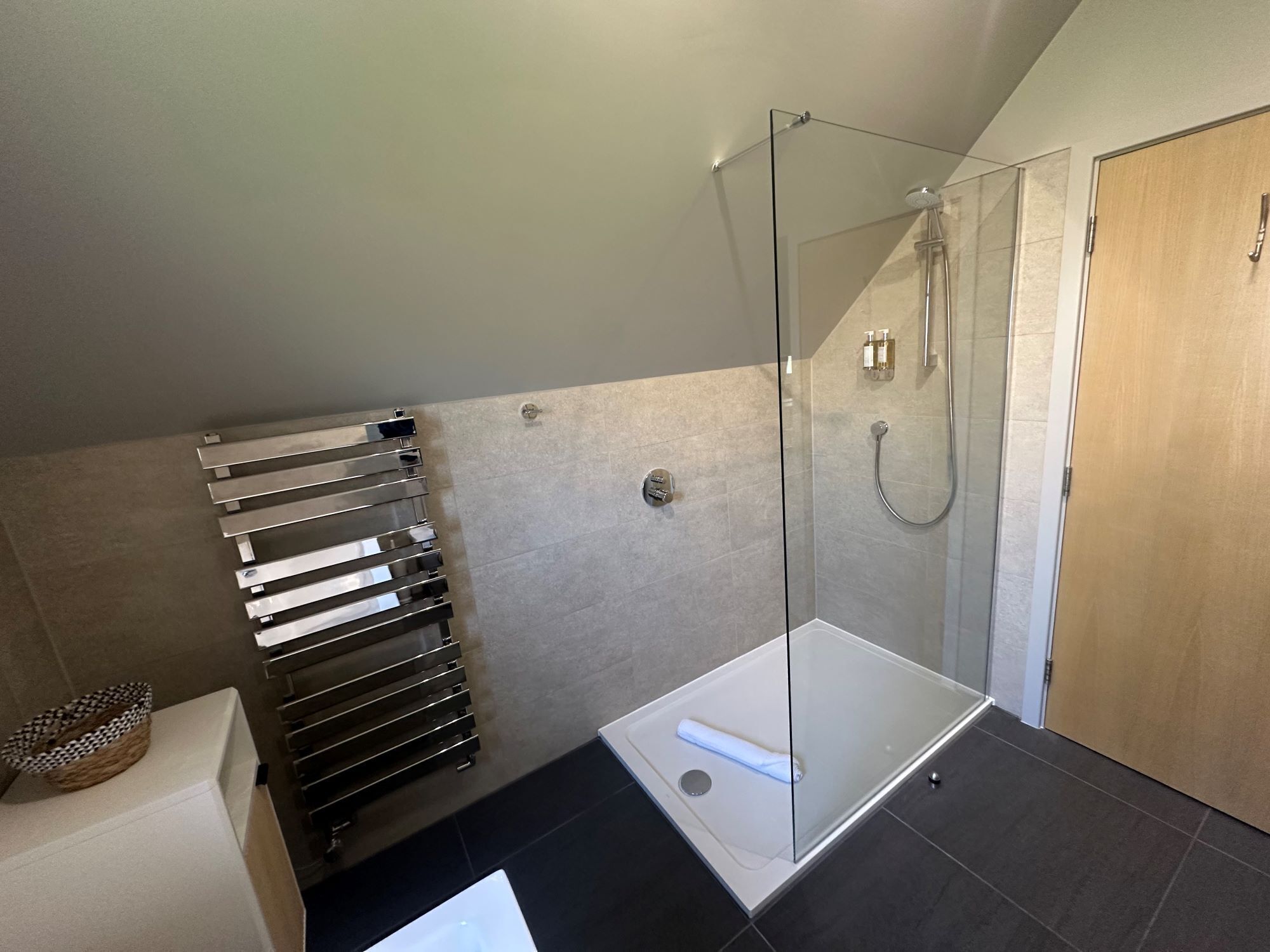 A modern bathroom with a glass-enclosed shower, a white bathtub, and a towel rack.