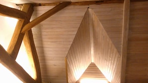 Ein Zimmer mit Holzbalken, einer geneigten Decke, einem Fenster mit Ausblick und einer Pflanze in der Ecke.