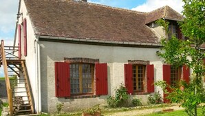 Ein zweistöckiges Haus mit einem geneigten Dach, roten Fensterläden und einer Holztreppe zum Eingang.