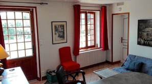 Ein Zimmer mit einem roten Sessel, einem blauen Sofa, einem Heizkörper und einem Fenster mit roten Vorhängen.