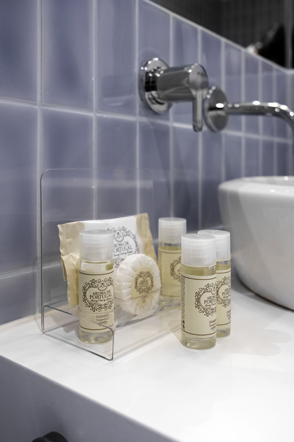 Une salle de bain avec une étagère transparente où sont rangés les articles de toilette, un lavabo blanc et un mur recouvert de carreaux bleus.