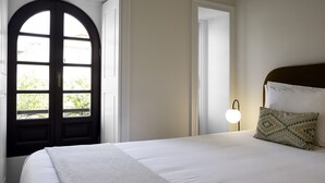 Une chambre avec une grande fenêtre en arc de cercle, un lit recouvert de draps blancs et une lampe de chevet.