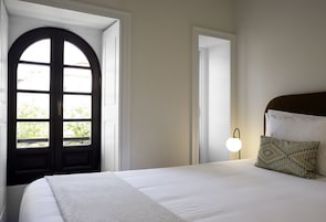 A bedroom with a large arched window, a bed with white linens, and a bedside lamp.