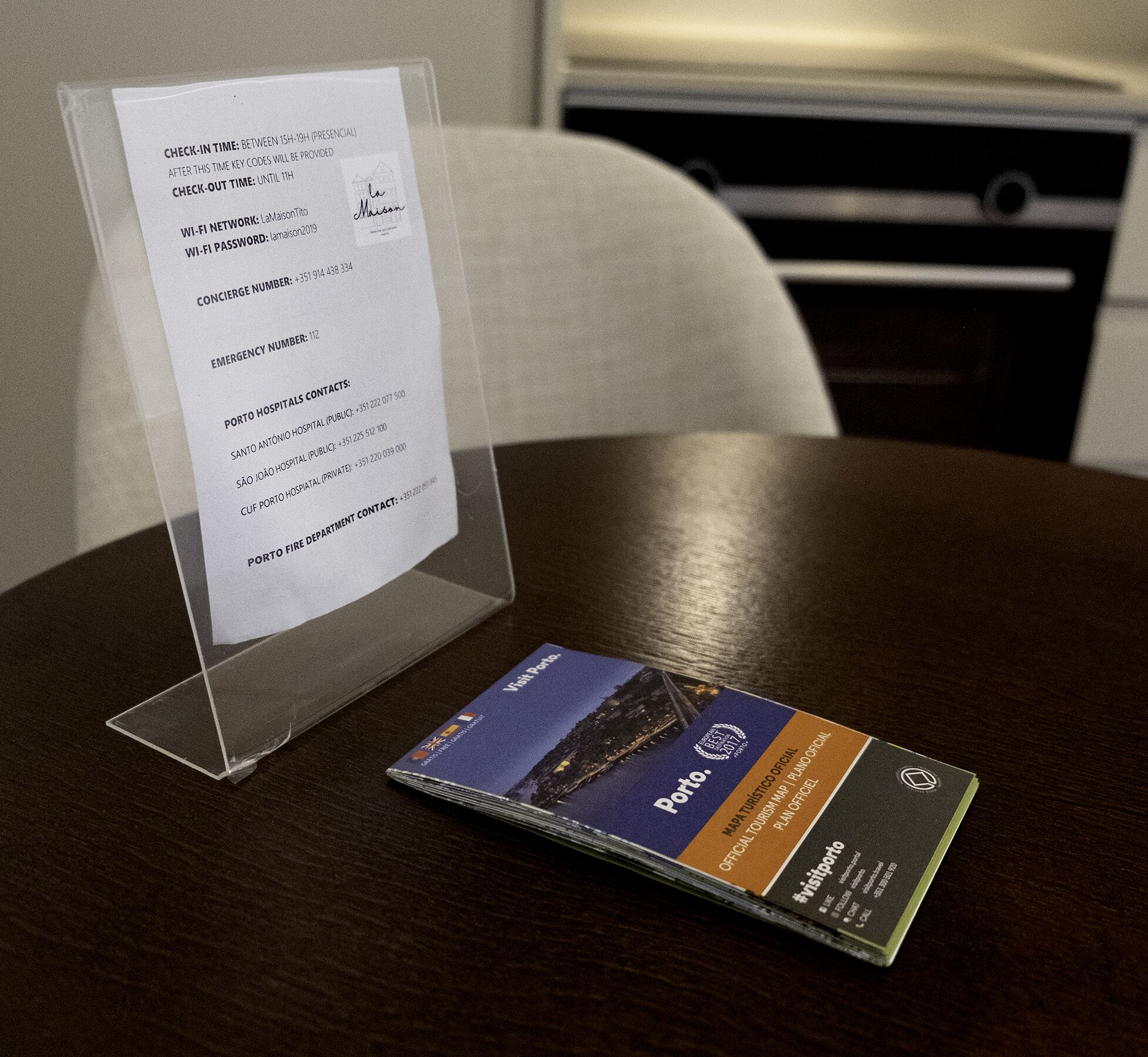 Een hotelkamer met een transparante plastic standaard waarop een welkomstkaart en een brochure liggen op een houten tafel.