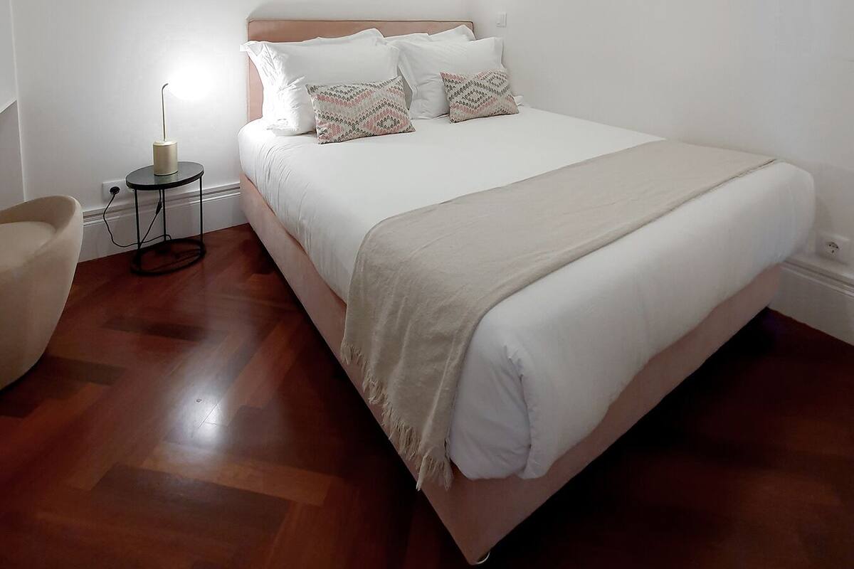 A bedroom with a large bed, a round mirror, and a bedside table with a lamp.