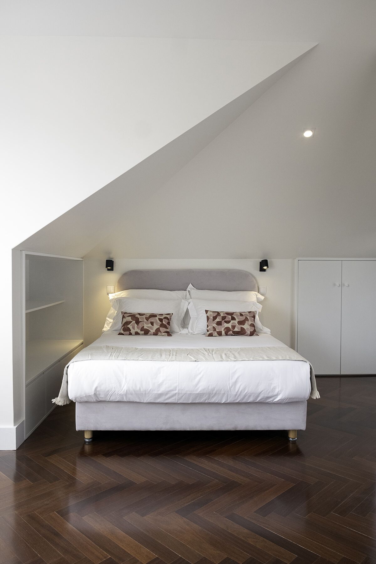 Una camera da letto con un letto grande, due lampade ai comodini, un armadio e un soffitto spiovente.