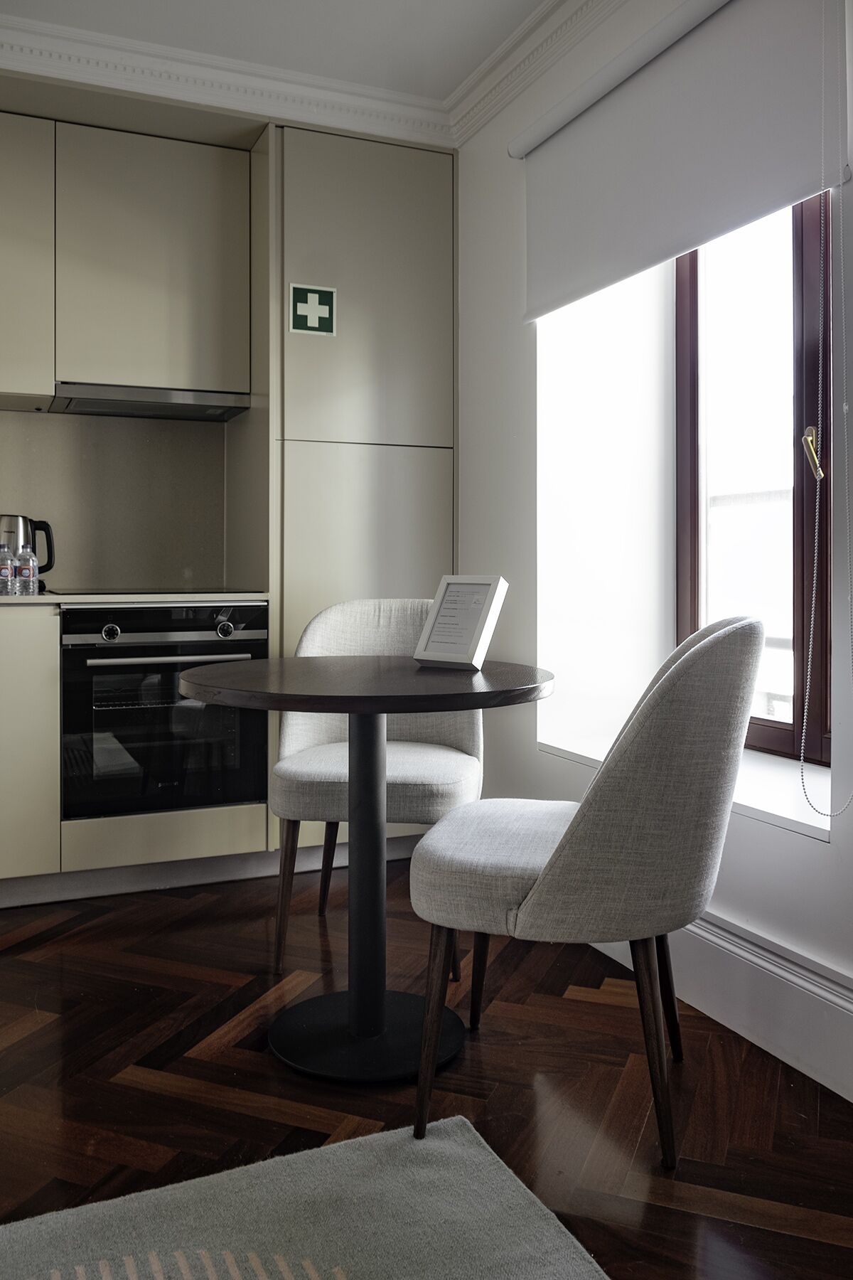 A modern kitchen with a dining area, a medical first aid sign, and a window with a view.