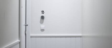 Un couloir aux murs blancs, doté d’un plancher en bois, d’une porte et d’un luminaire fixé au mur.