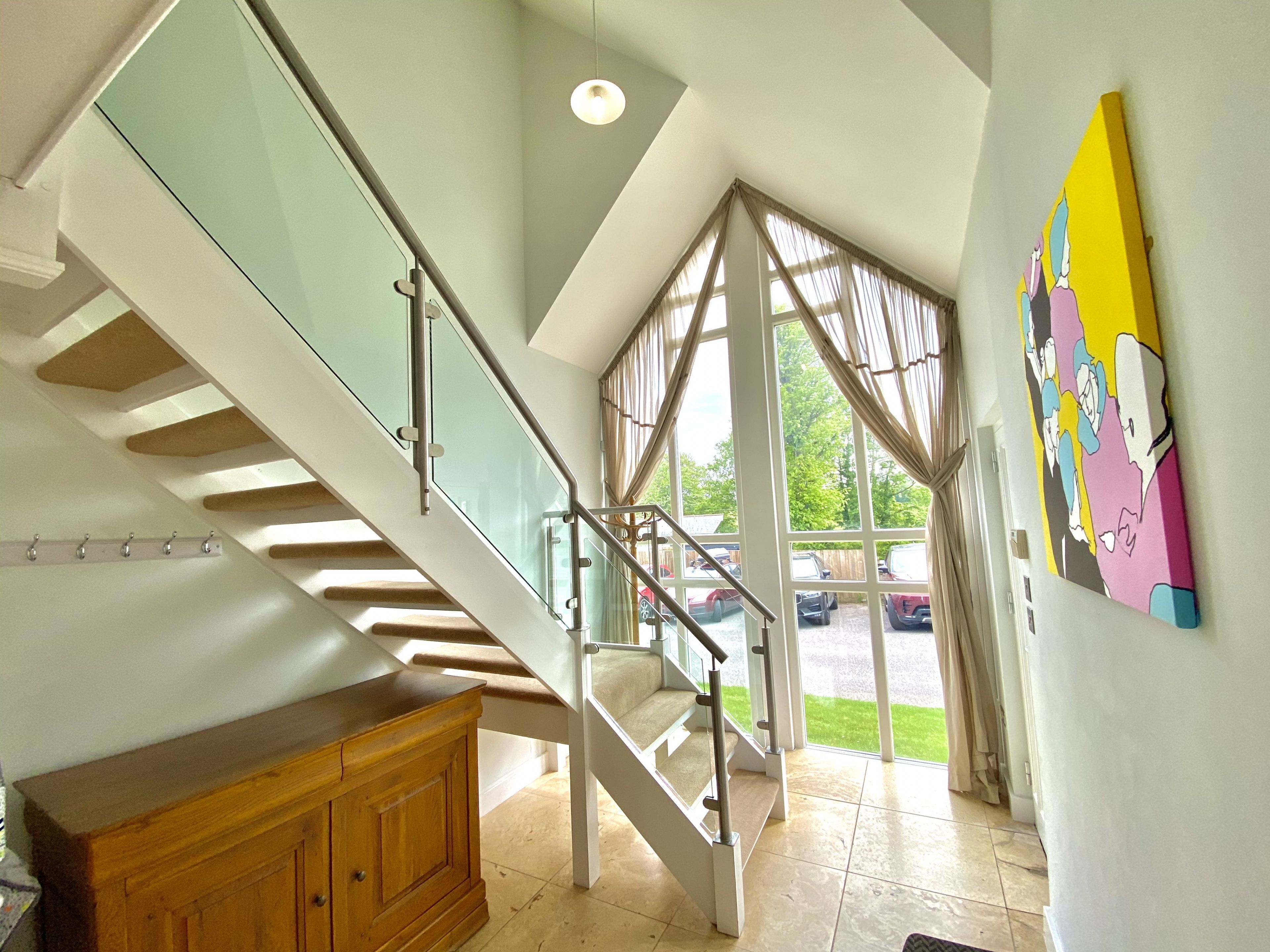 A modern staircase with glass railings, a wooden cabinet, and a colorful painting on the wall.