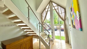 A modern staircase with glass railings, a wooden cabinet, and a colorful painting on the wall. - Trewhiddle Villa 2 -  a trewhiddle that sleeps 7 guests  in 4 bedrooms (Saint Austell)